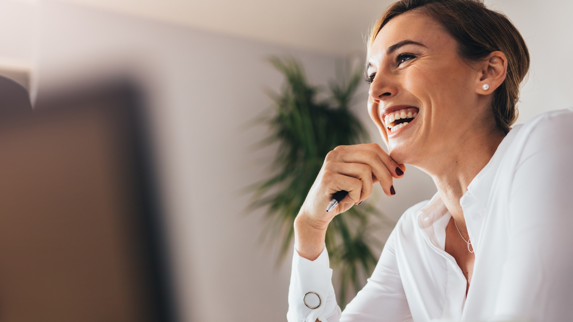 A woman looking happy at her desk with a pen in her hand.