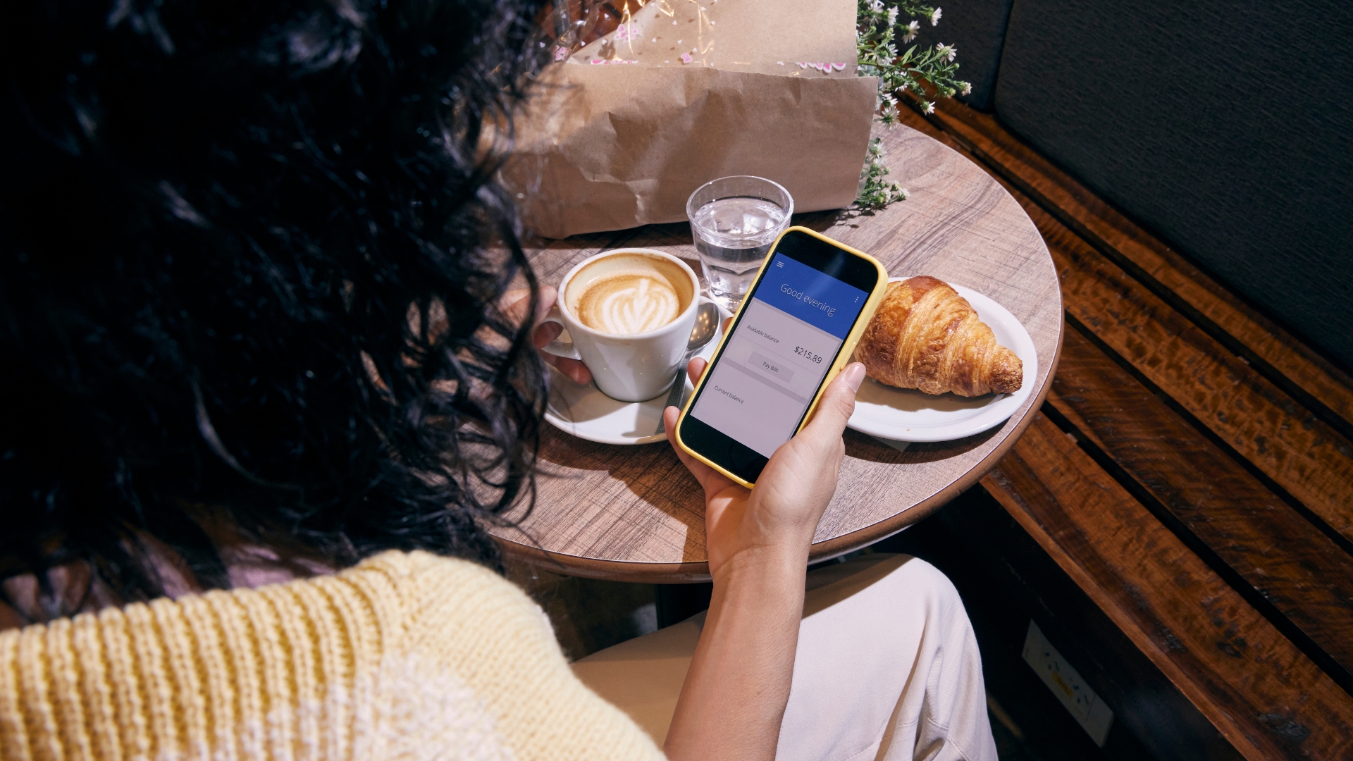 Woman looking at bank accounts on her cellphone with a pastry and coffee in the background.