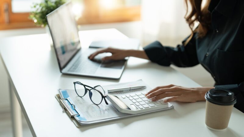 Mujer en su escritorio con gafas en un cuaderno, haciendo planificación financiera 