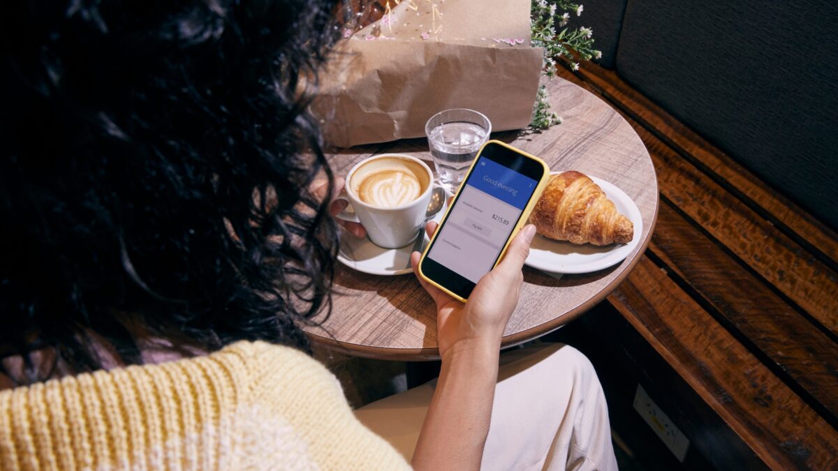 Woman looking at bank accounts on her cellphone with a pastry and coffee in the background.